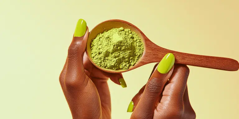 Close-up of hands holding a wooden spoon with green kratom powder, symbolizing natural energy, relaxation, and wellness benefits from high-quality kratom.